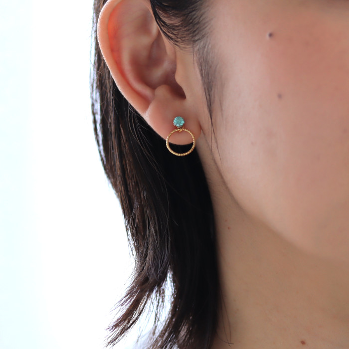 シャンパンゴールドリングチャームとサファイアグリーンのピアスを耳に着けた女性の耳元画像