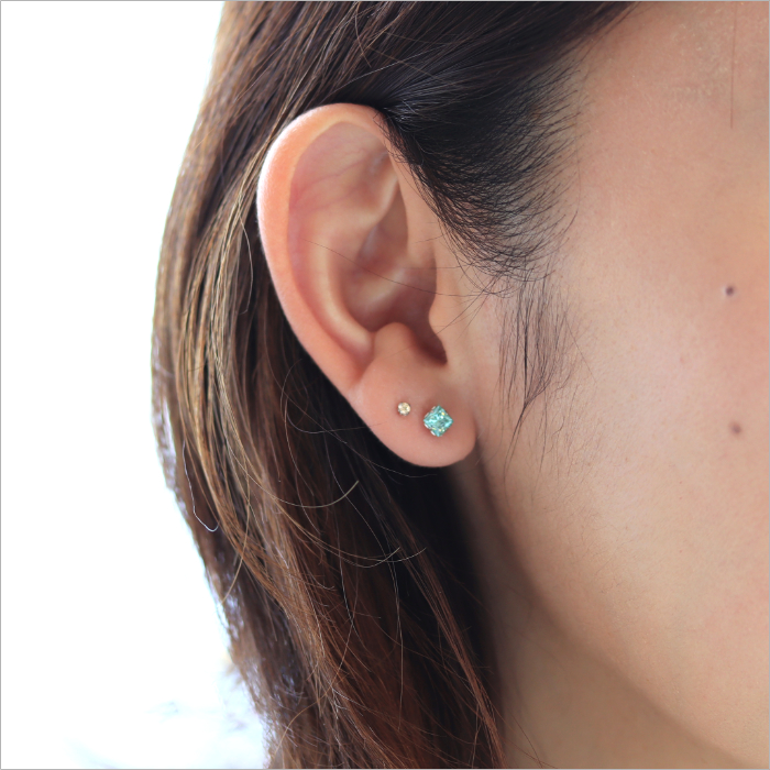 四角いサファイヤグリーンのピアスと小粒のシャンパンダイヤのピアスを着けた女性の耳元画像