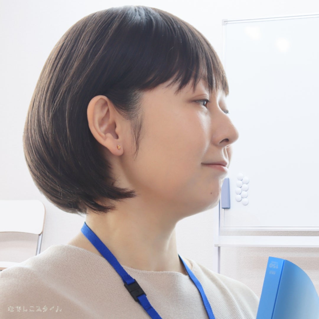 ゴールドカラーのキンモクセイピアスをつけてお仕事をする女性の画像